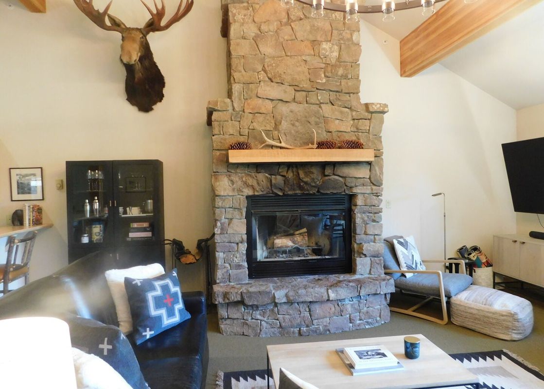 The spacious living area at Moose Creek 35 boasts a grand stone fireplace, a large moose head mounted above, and comfortable seating with modern and rustic decor.