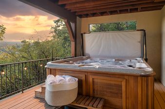 A private outdoor deck at the Valley View Retreat with a steaming hot tub, offering scenic views of a valley and sunset.