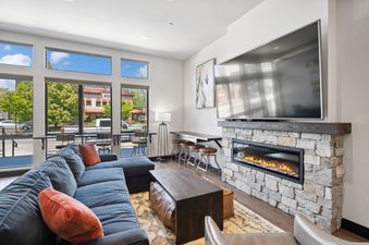 A modern and inviting living room featuring a large gray sectional sofa with orange pillows, a dark wood coffee table, and a stone fireplace with a mounted flat-screen TV.