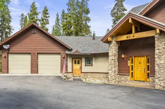 The Grand View on the Blue exterior with garages, stone, and wood finishes, surrounded by evergreen trees.