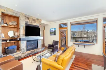 A spacious living room at Granita 303 2BR 2BA with a stone fireplace, flat-screen TV, and comfortable seating, all overlooking a stunning mountain view.