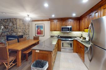 The kitchen in Manor Vail 118 features a stone accent wall, stainless steel appliances, and a large dining table.