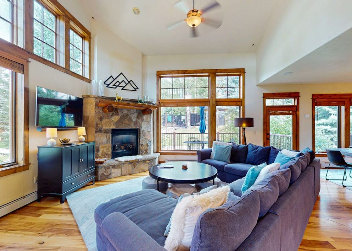 A spacious and bright living room at EagleRidge Townhomes 1510 featuring a blue sectional sofa, a stone fireplace, and large windows with scenic views.