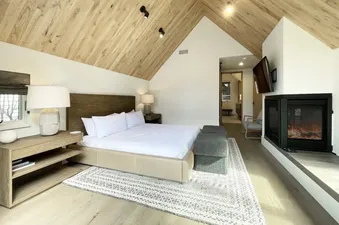The master bedroom at Loft House 101 at Transfer, featuring a large king-size bed with white linens, a wood-burning fireplace, and a view of the snow-capped mountains.