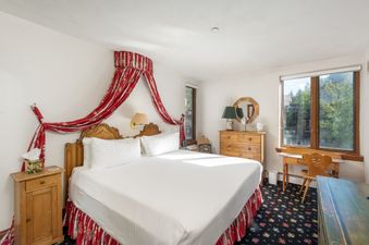 A cozy bedroom with a large bed, wooden furniture, and a window offering an exterior view.