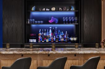 A bar counter with a row of bottles on the back shelf and bar stools in the foreground.
