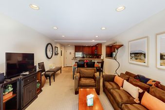 A living room with a brown suede couch, a large flat-screen television, and a clock hanging on the wall.
