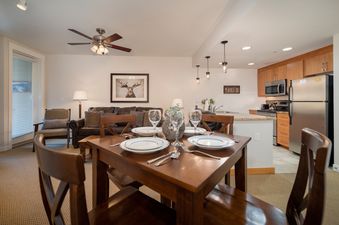 The dining area and kitchen are visible, with a living room in the background.