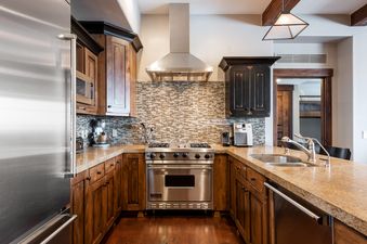 A modern kitchen with stainless steel appliances, wood cabinets, granite countertops, and a mosaic tile backsplash.