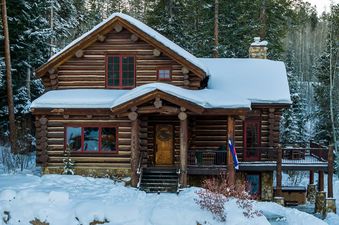 The Moose Drool Lodge is a charming log cabin with snow-covered roofs and surrounding pine trees, showcasing its rustic elegance in a winter wonderland.