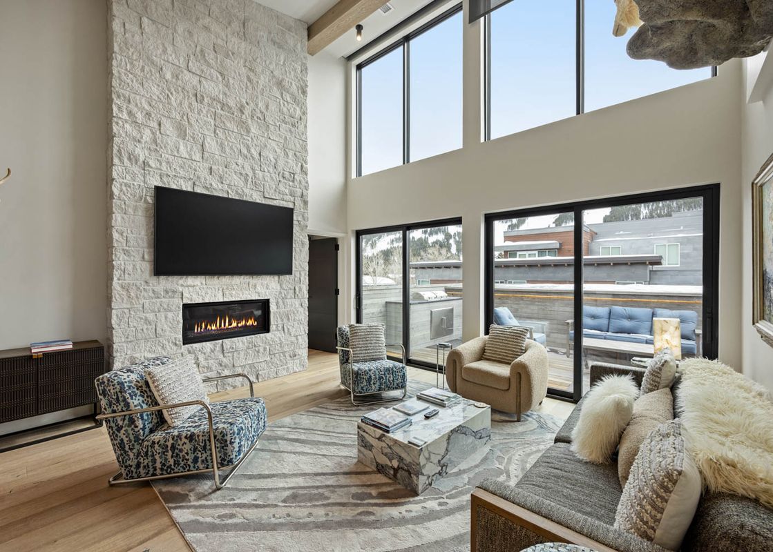 Luxurious living room featuring a grand white stone fireplace, modern furnishings, and large windows with outdoor views.