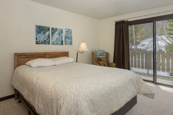 The bedroom at Hideaway Village Alpine 4 features a wooden headboard, a white patterned comforter, and artwork on the wall.