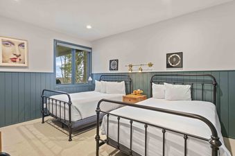 A cozy bedroom in Twin Pines 6 featuring two twin beds with dark metal frames, teal-paneled walls, and a window with a nature view.