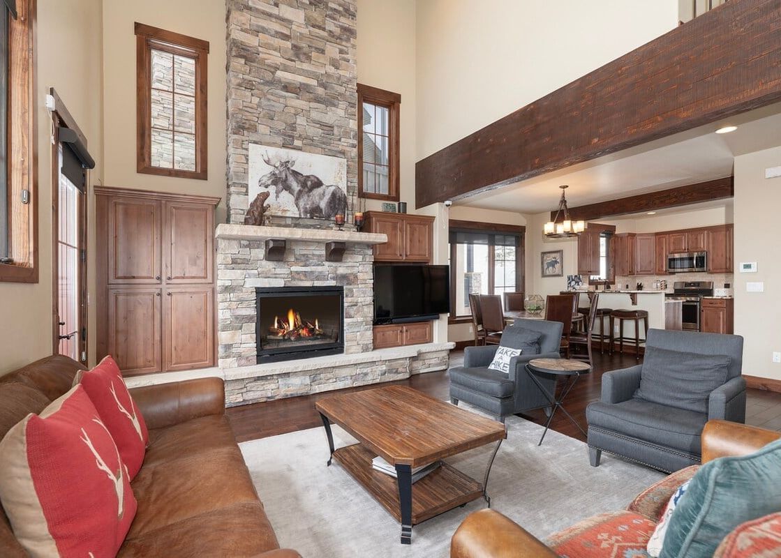 The grand living area of 751 Mountain Terrace features a stunning stone fireplace, comfortable seating, and an open-concept design flowing into the kitchen and dining areas.
