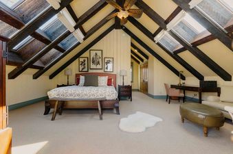 The attic bedroom at Elk Lake Lodge features a bed, a desk, a sofa, and skylight windows, with a ceiling fan overhead.