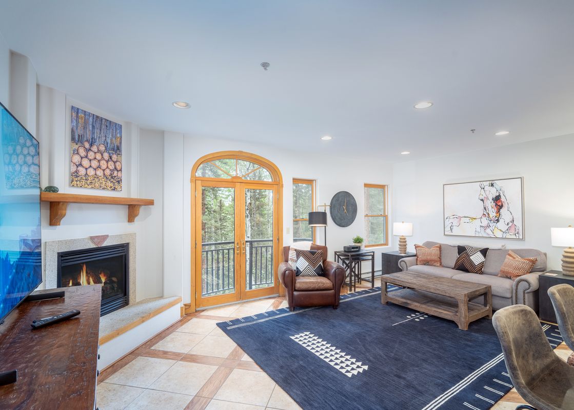 The living room in Bear Creek Lodge 202 features a fireplace, a leather armchair, a couch, a coffee table, a rug, and a view out of a french door