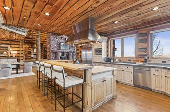 The Treehouse in Canyons Village kitchen has an island with seating, stainless steel appliances and wooden cabinetry. There is a large window offering a view of the surrounding mountains.