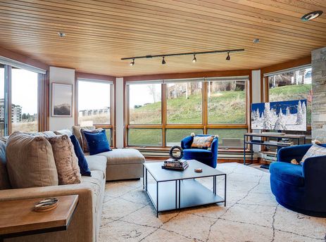 An inviting lounge at Chateau Chamonix CX211 with a large sectional sofa, blue velvet accent chairs, a black coffee table, and expansive windows offering scenic views.