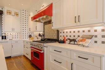 A modern kitchen with vibrant red appliances, white cabinetry, and patterned tile backsplash, featuring a Viking range and a stylish design.