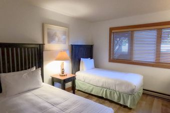 A cozy bedroom in Nez Perce D1 featuring two twin beds, a wooden nightstand with a lamp, and a large window with wooden blinds.