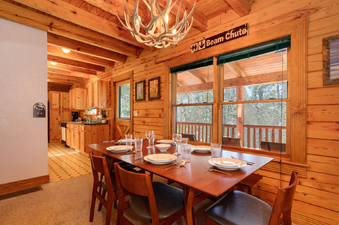 A rustic log cabin dining area and kitchen are illuminated by a unique antler chandelier.