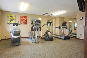 A well-equipped fitness center with various exercise machines, including a treadmill, elliptical, and Stairmaster, with colorful artwork on the walls.