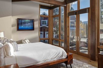 A bedroom with a king-sized bed, a large picture window overlooking a forest, and a wood-burning fireplace.