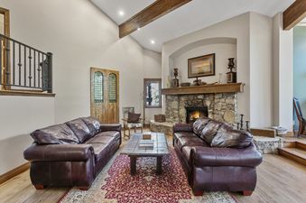 A living room with two brown leather sofas, a coffee table, a rug, a fireplace, and large windows.