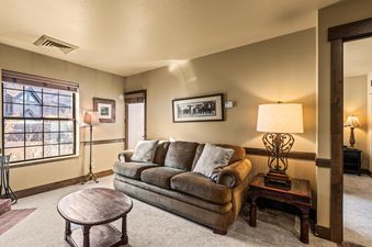 A cozy living room at Copperbottom Inn 103 with a brown sofa, coffee table, and a large window overlooking an outdoor view.